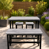 Outdoor gray wooden dining table with matching benches in a sunlit garden patio, lavender and greenery in the background.